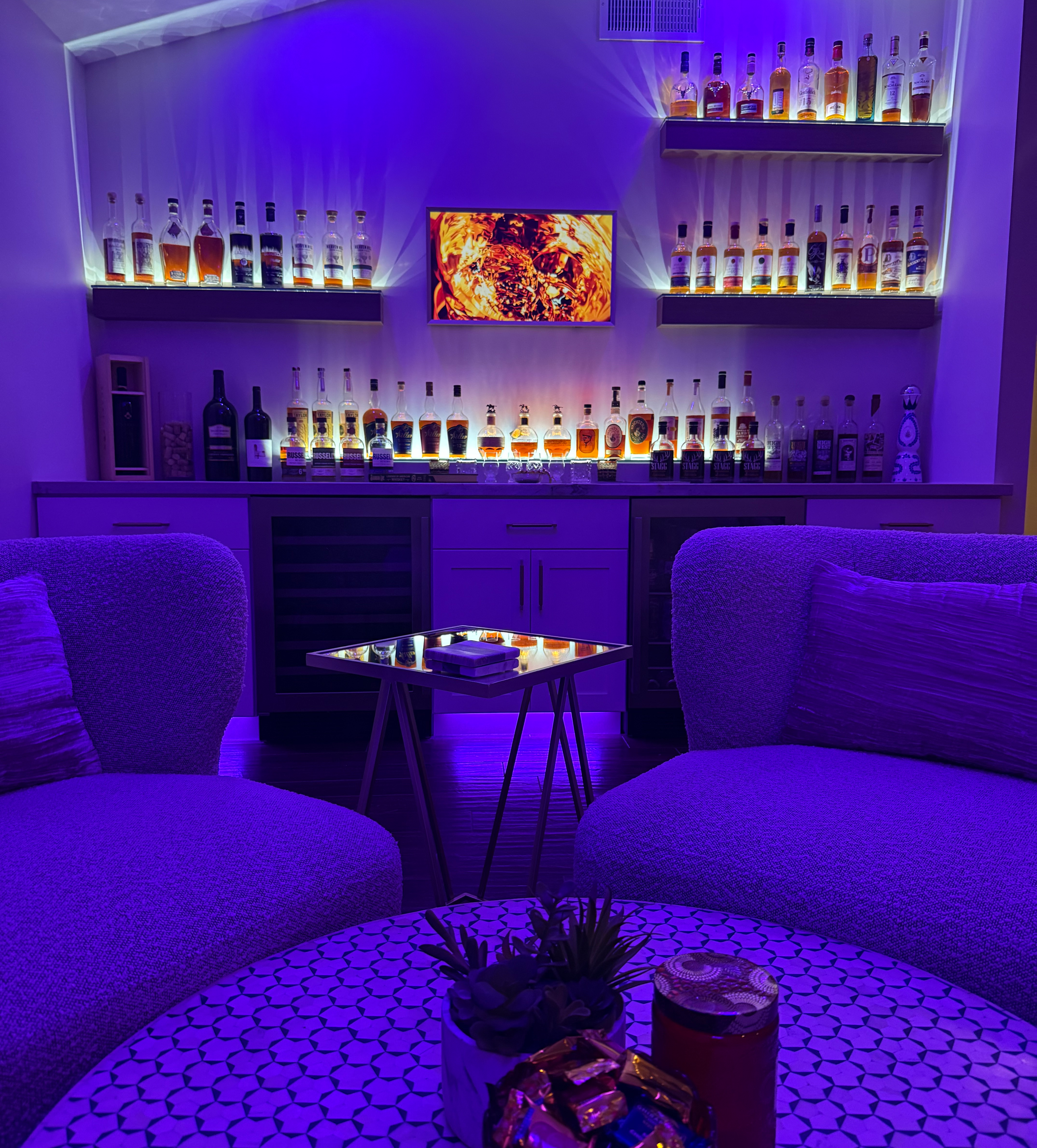 Integrated LED bar shelves illuminating a home bar with liquor bottles and ambient purple lighting